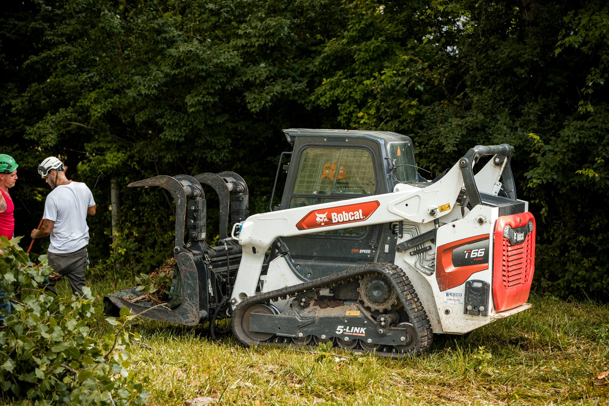 Compact loader carrying cut brush across a pasture
